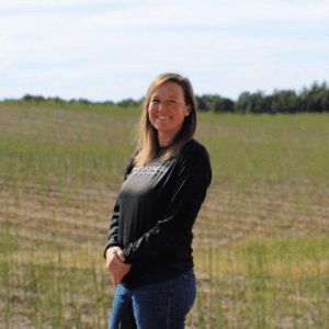 Headshot featuring a woman in a black long-sleeved shirt standing in a field and smiling at the camera