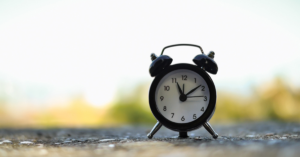 Image of a old-fashioned wind up alarm clock on the ground with a blurred background.
