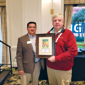 Man in brown sport coat, left, presents a framed award to man in a red pullover sweater