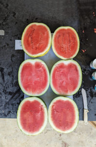 Three large watermelons split in half, resting on a board