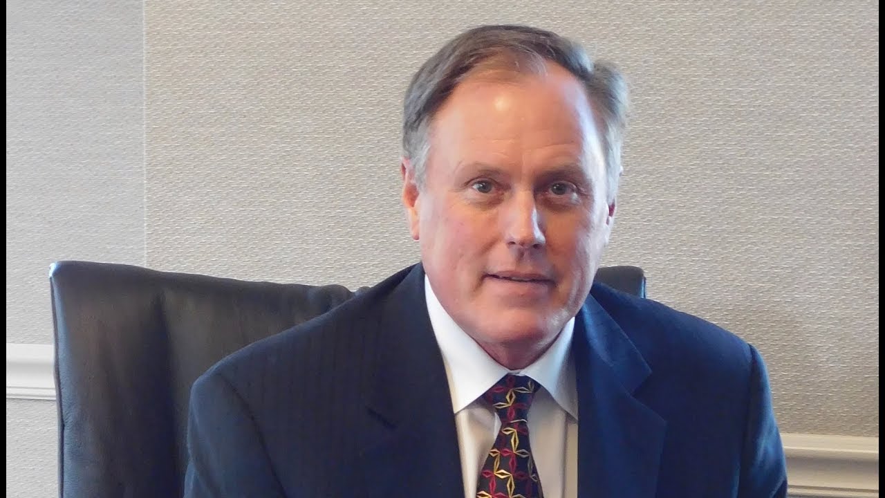 Photo of a man with a patterned tie and a blue suit jacket sitting in a black chair