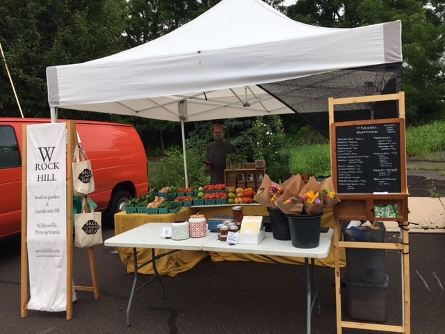 Farmers market booth, with a white canopy and multiple tables with products, as well as signs on each side